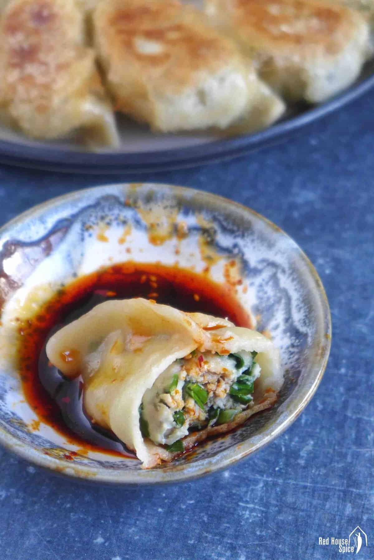 a half-eaten pork and chive dumpling in dipping sauce.