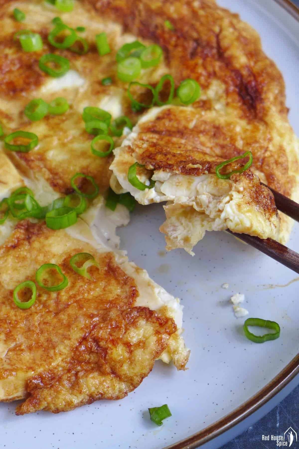 chopsticks picking up a piece of tofu omelet.