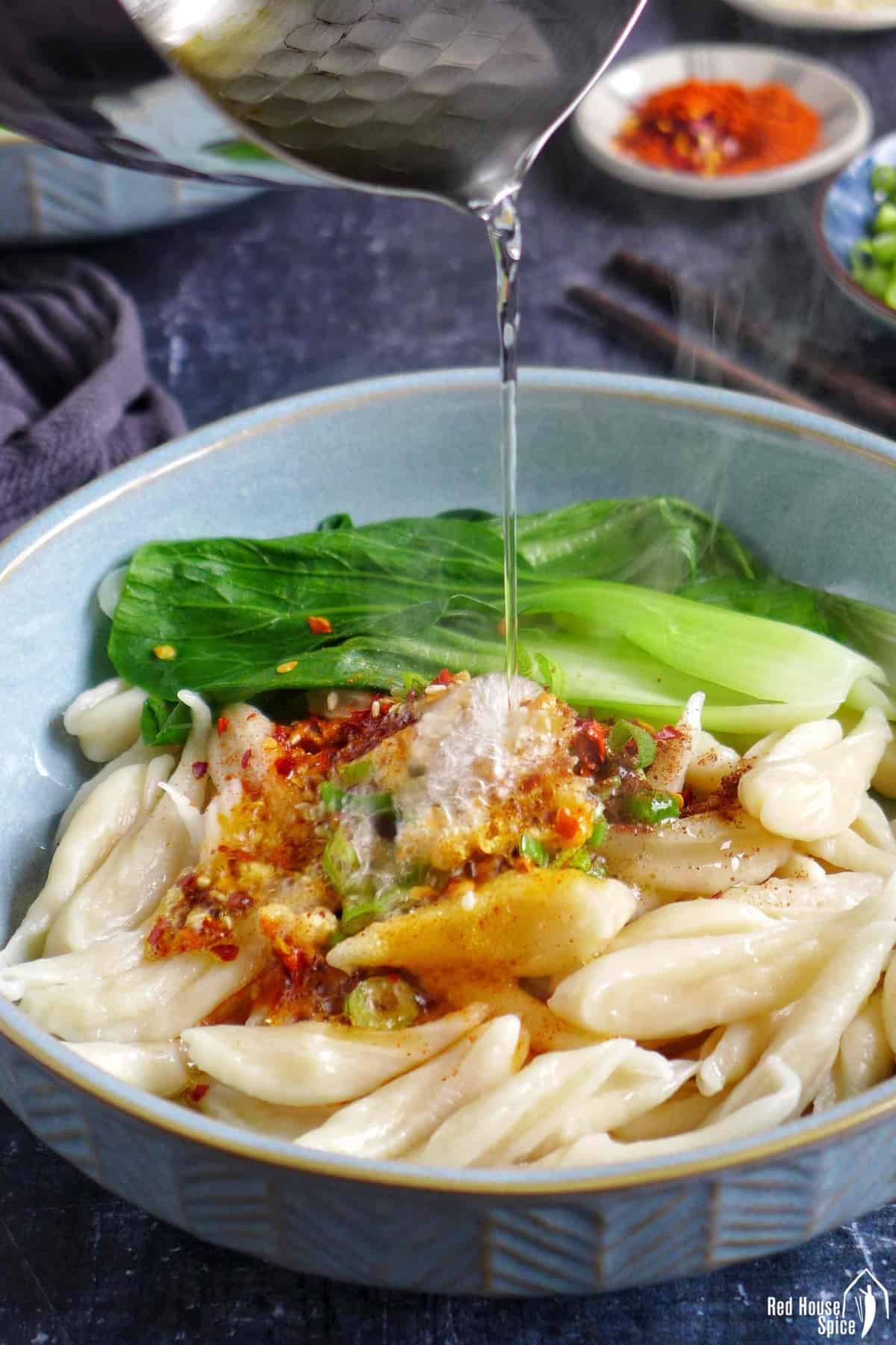 Pouring hot oil over spices in a noodle bowl