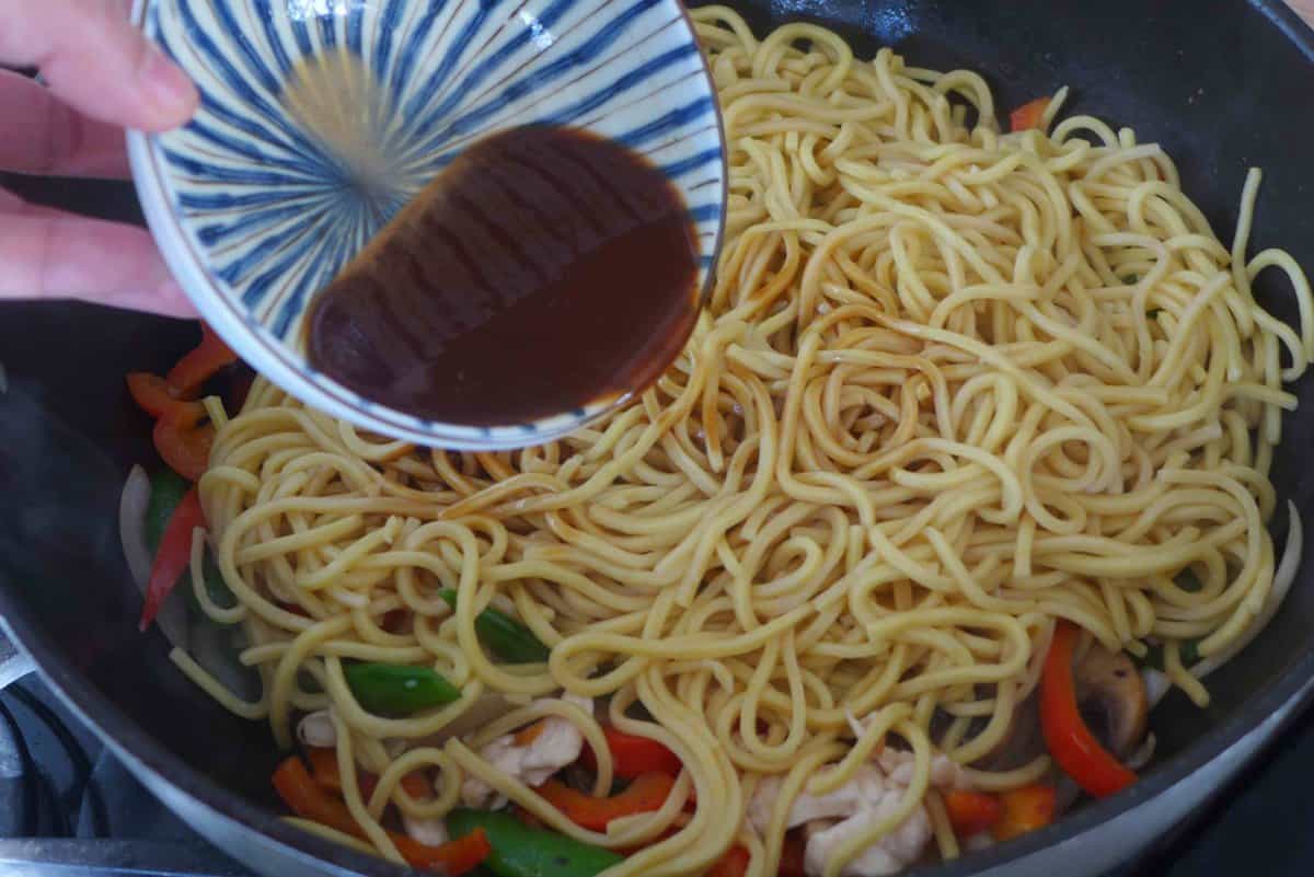pouring lo mein sauce over noodles and vegetables.
