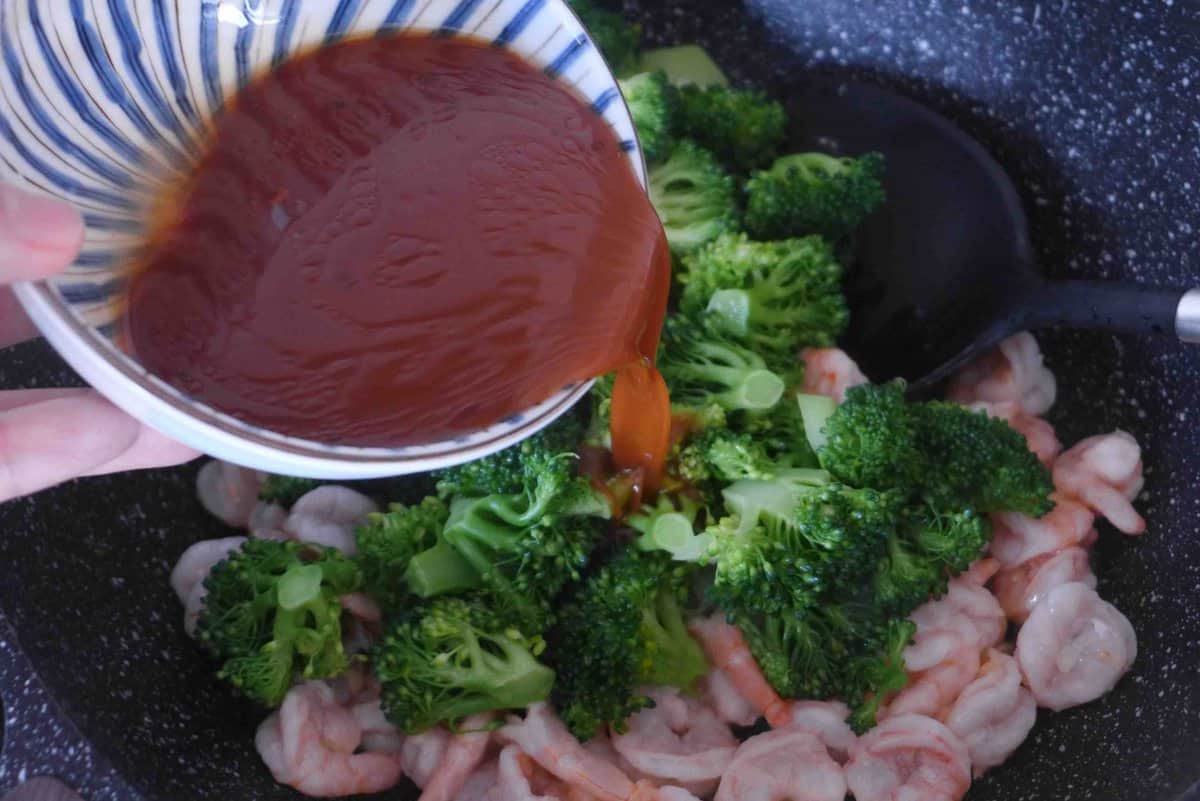 pouring sauce over broccoli and shrimp.