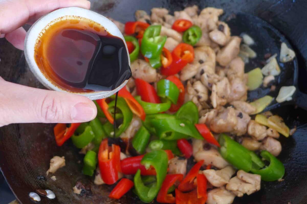 adding soy sauce to chicken and chili peppers.