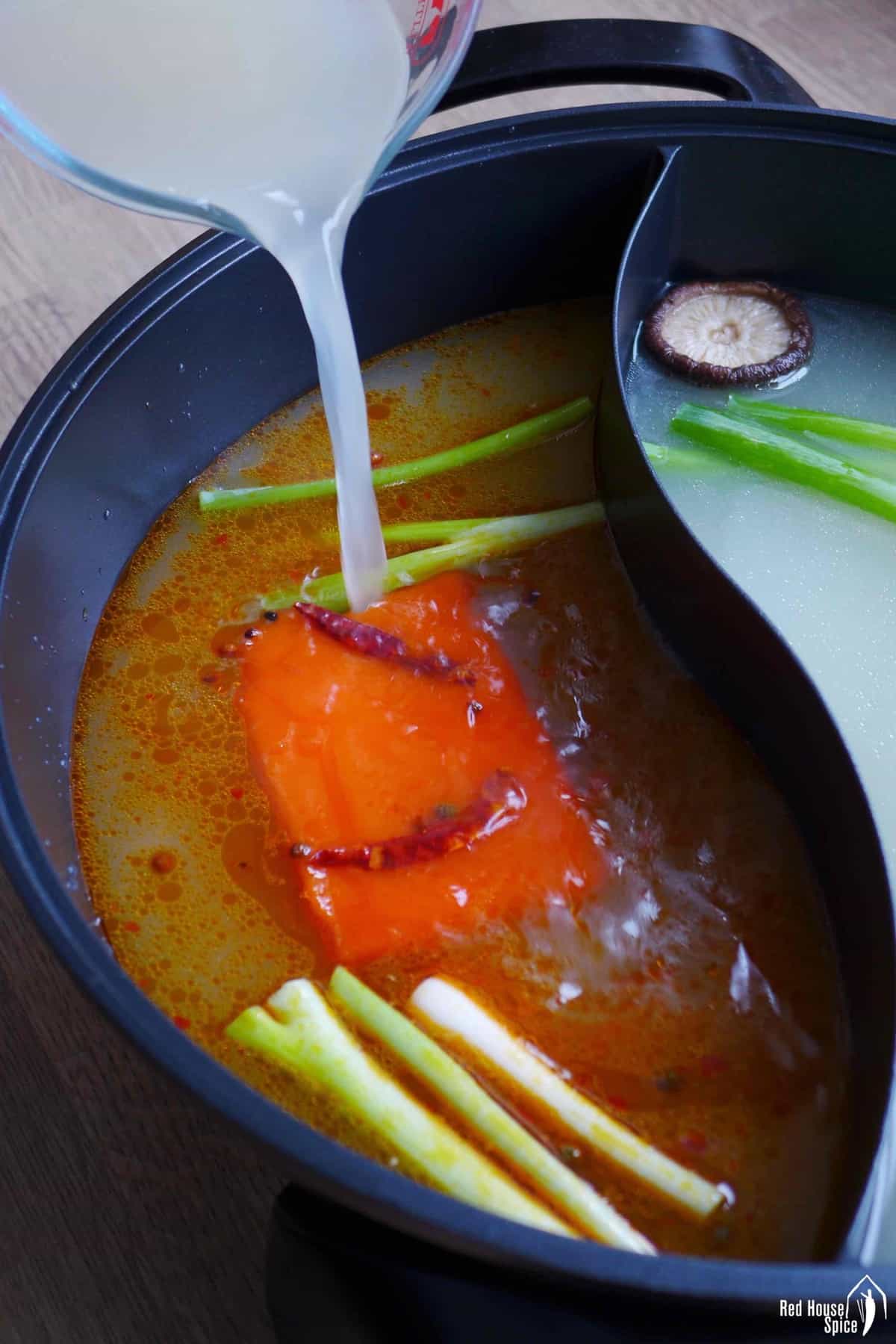 pouring stock over spicy soup base block