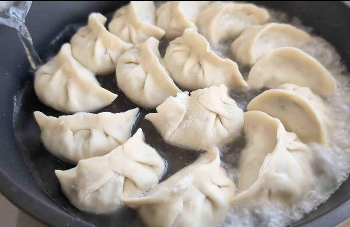 pouring water into skillet filled with dumplings.