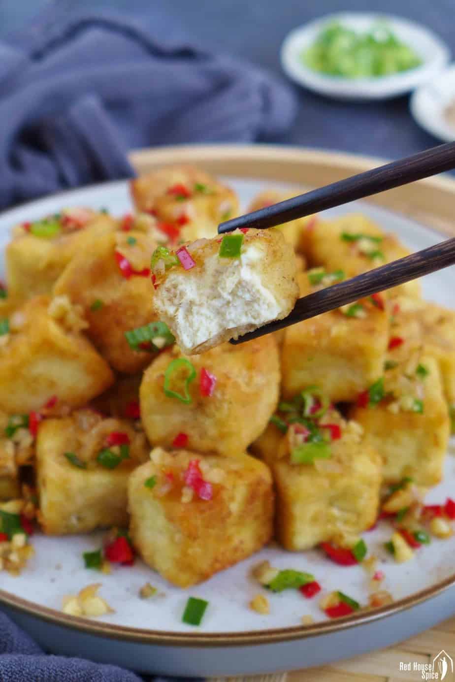 chopsticks picking up a piece of half eaten fried tofu