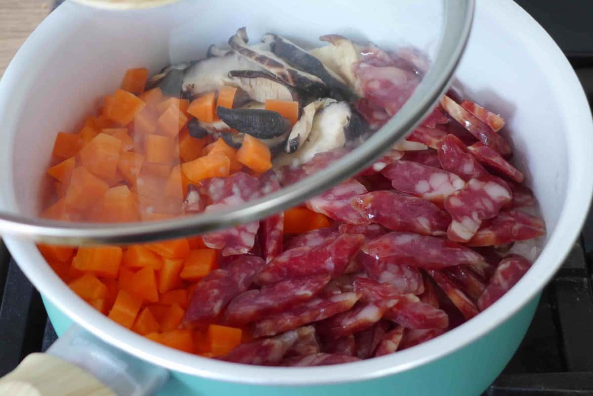 uncooked Chinese sausages, carrots and mushrooms over rice in a saucepan.
