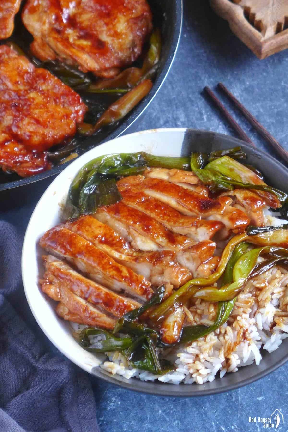 scallion chicken chops over steamed rice. with uncut chicken in skillet.