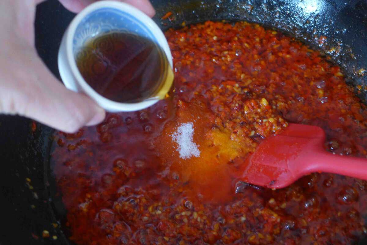 Adding sesame oil to fried peppers.