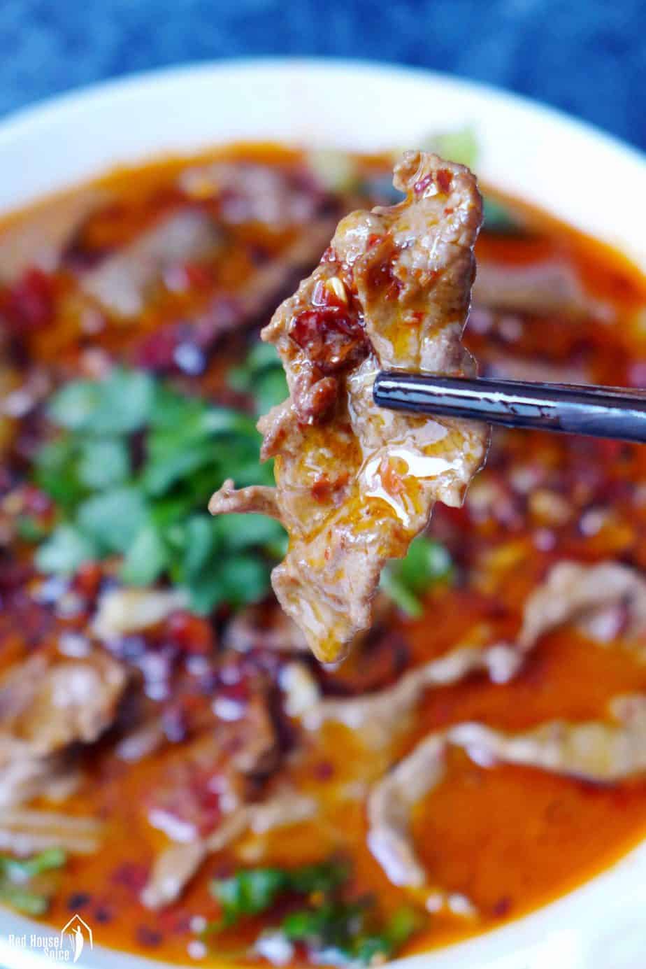 A piece of Sichuan boiled beef held by chopsticks