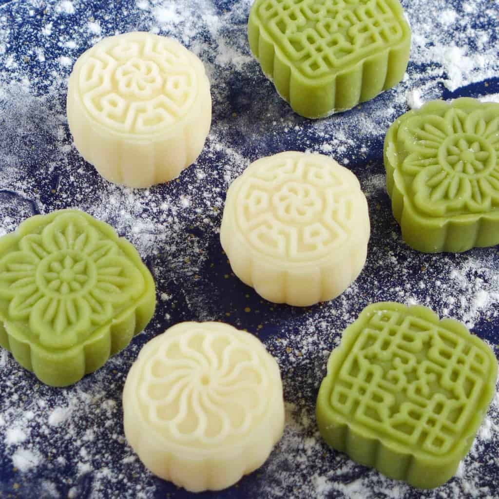white and green Snow Skin Mooncakes on a dusted surface.