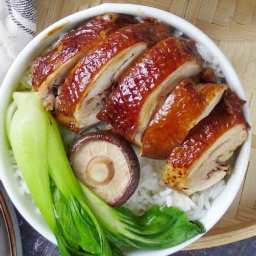 Soy sauce chicken over a bowl of rice with some vegetables