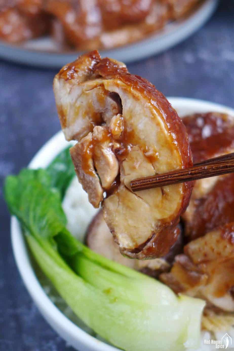 A piece of soy sauce chicken held by chopsticks