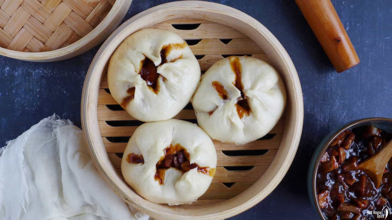 Three char siu bao in a bamboo steamer