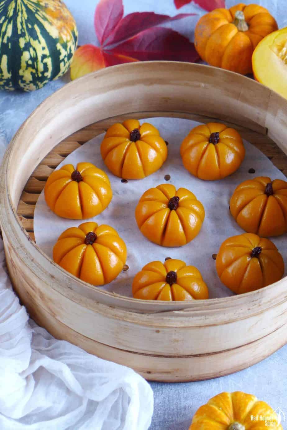 Steamed sticky rice pumpkin cakes in a steamer surrounded by winter squash and leaves.
