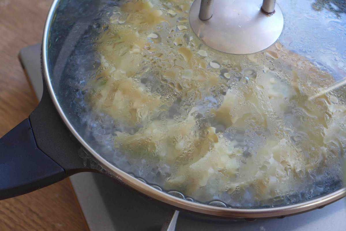 steaming dumplings in a skillet covered with a lid.