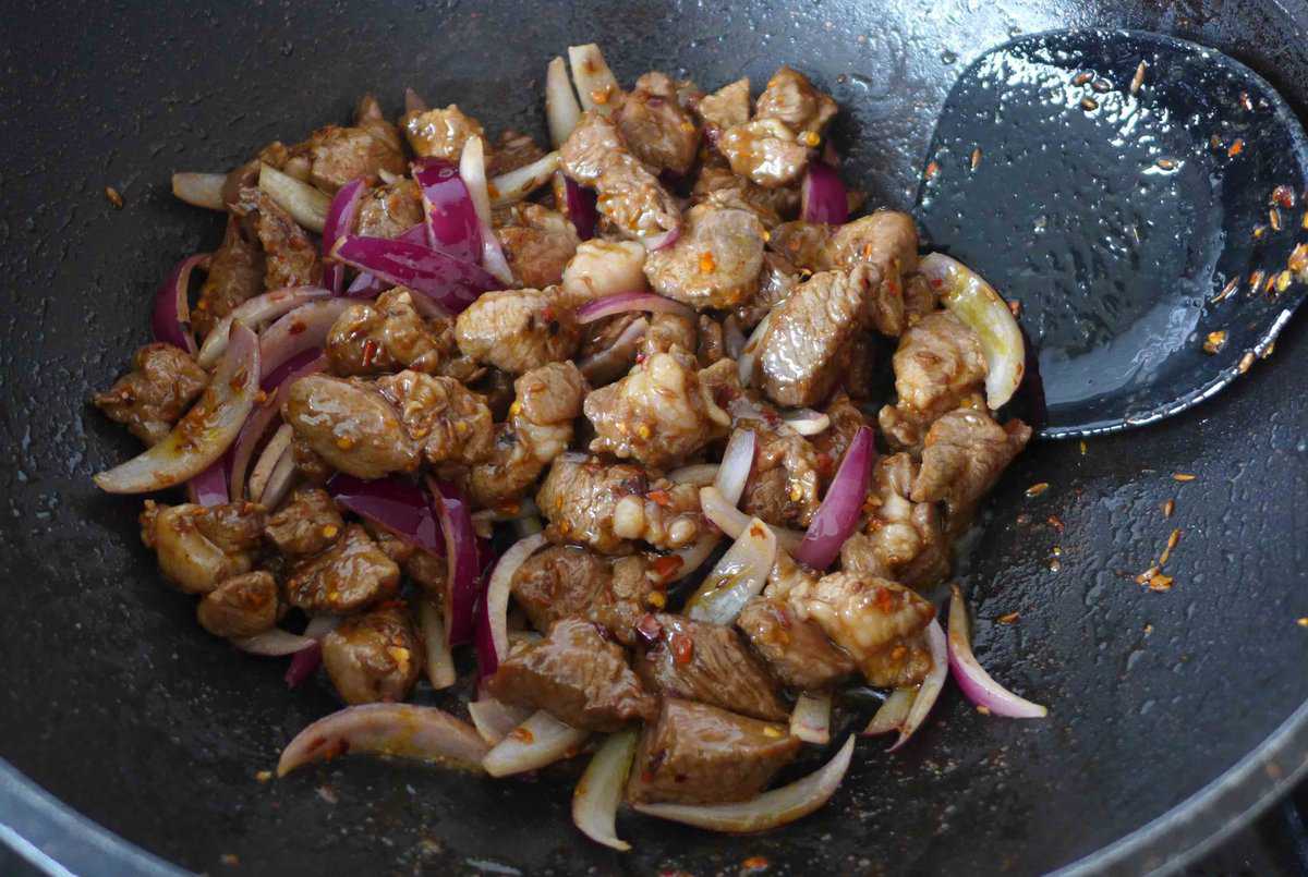 frying lamb cubes with sliced onion.