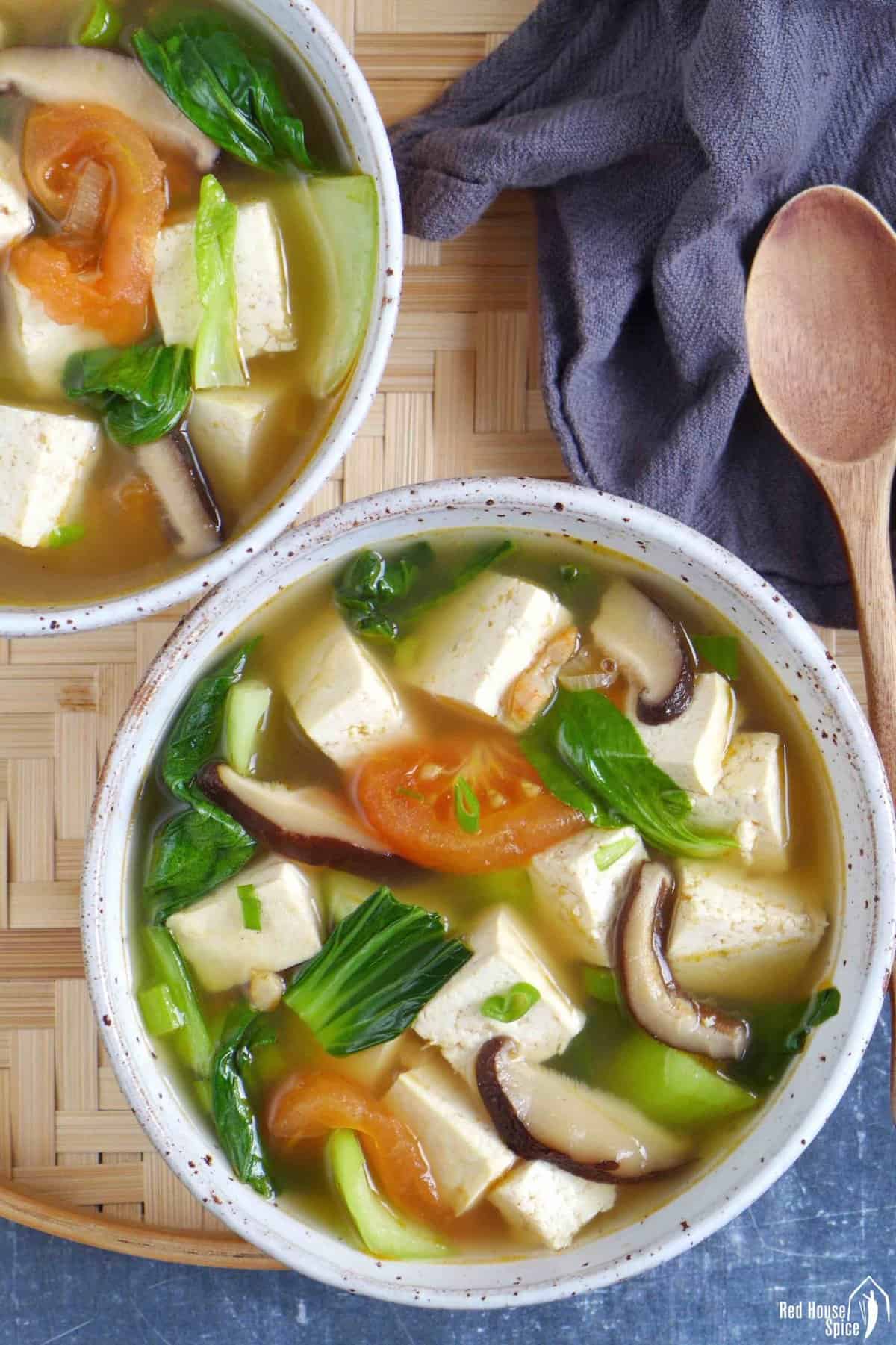 Two bowls of tofu soup with vegetables.