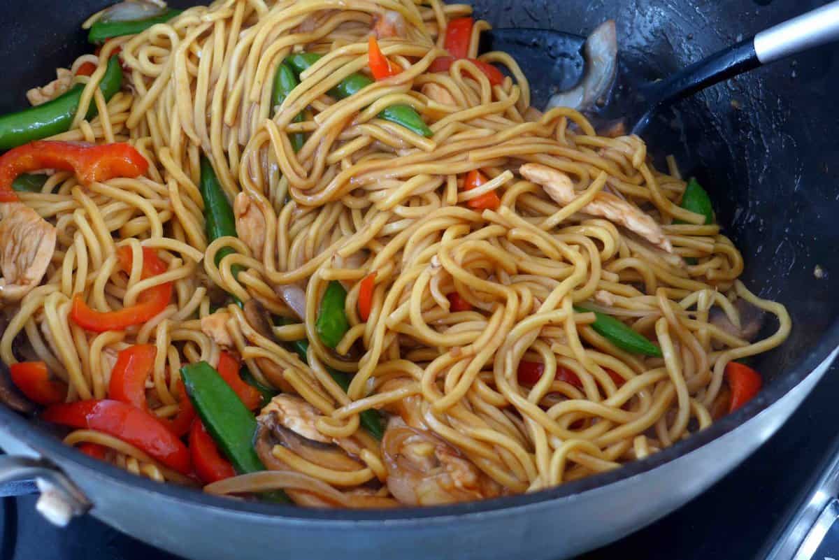 tossing noodles with chicken and vegetables.