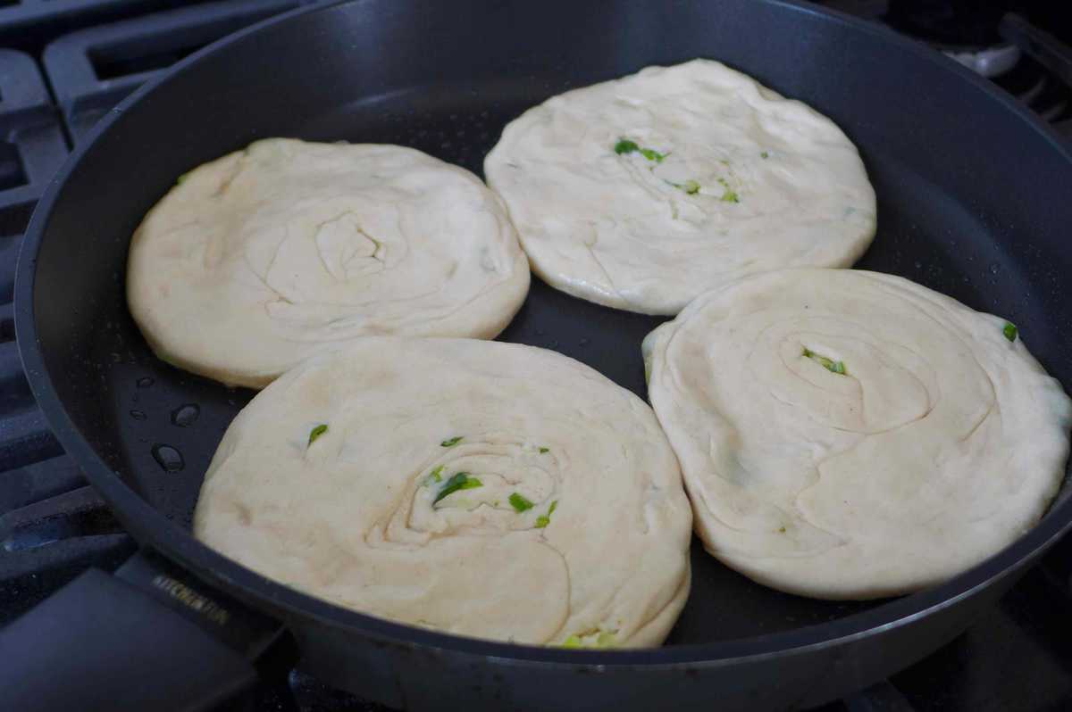four uncooked pancakes in a frying pan