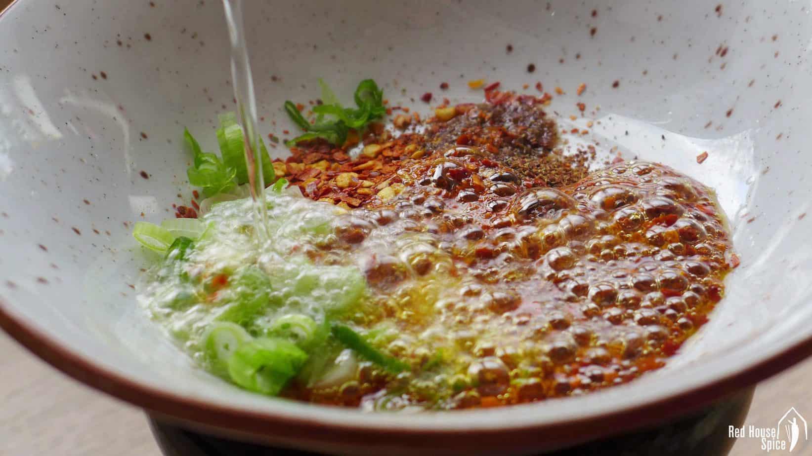 Hot oil pouring over chilli flakes and scallions.