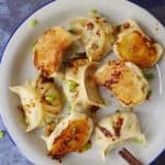 A plate of vegan dumplings covered with spicy sauce