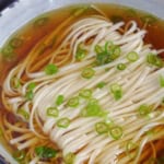 A bowl of Yang Chun Mian, noodle soup with clear broth and scallion garnish.