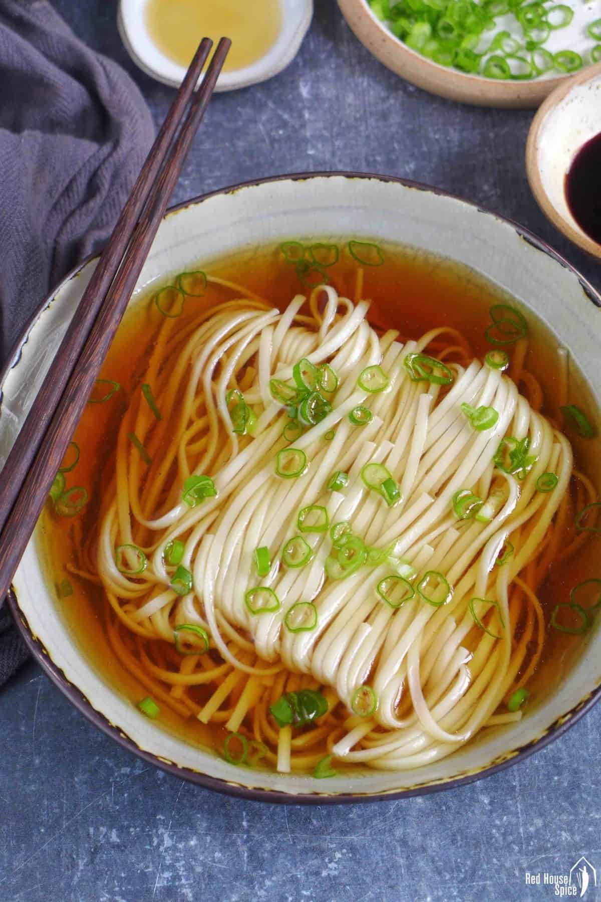 A bowl of noodle soup with clear broth and scallion garnish.
