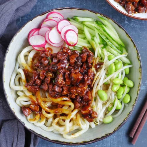 a bowl of Zha Jiang Mian, noodles with brown pork sauce and vegetable toppings.