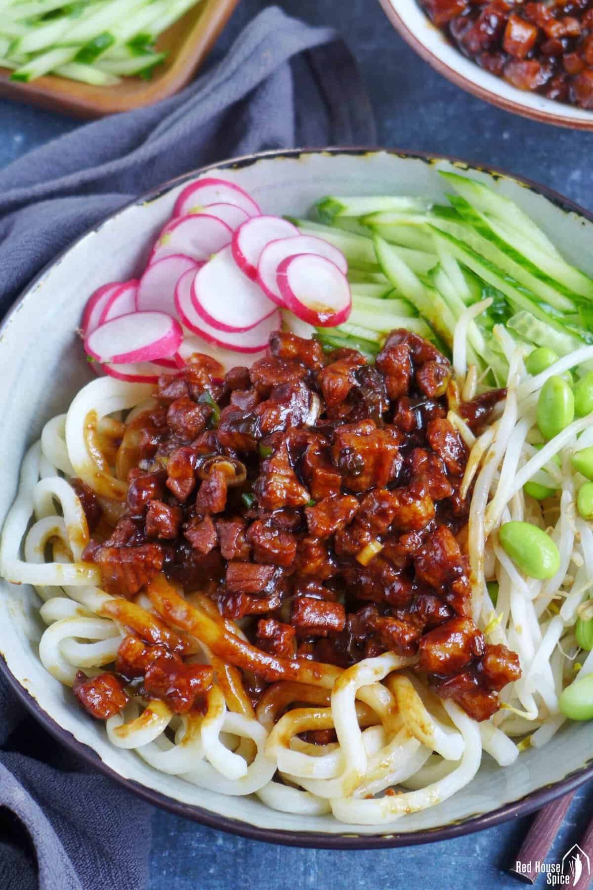 a bowl of Zha Jiang Mian, noodles with brown pork sauce and vegetable toppings.