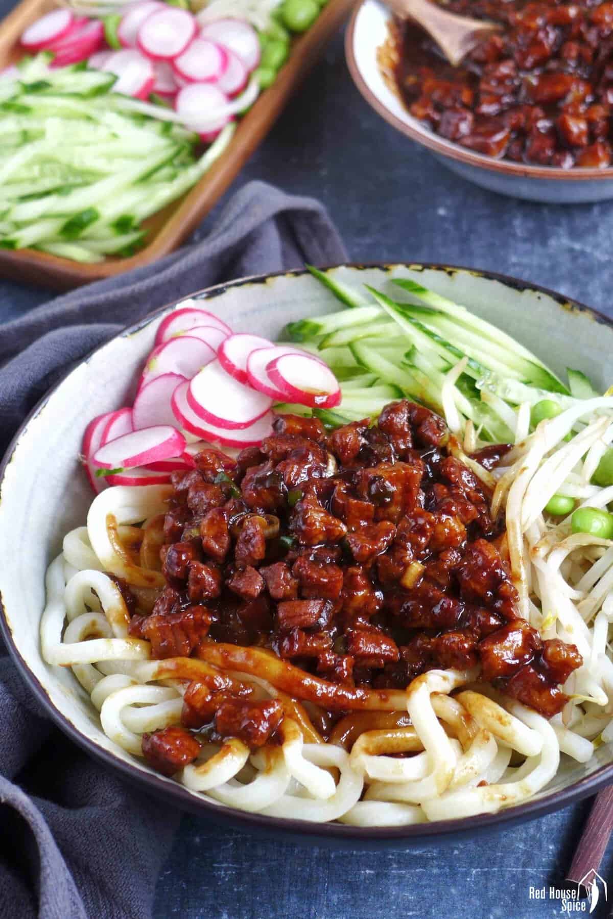 a bowl of Zha Jiang Mian, noodles with brown pork sauce and vegetable toppings.